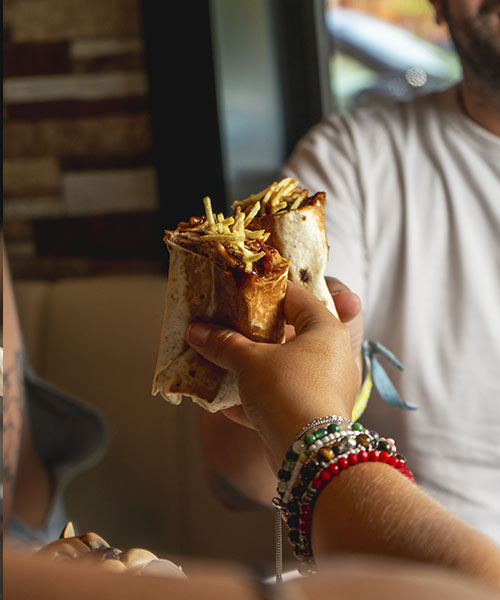 Fotografía lifestyle de manos brindando con burritos, producida por La Pecera para destacar marcas de comida urbana en un entorno cercano y auténtico.