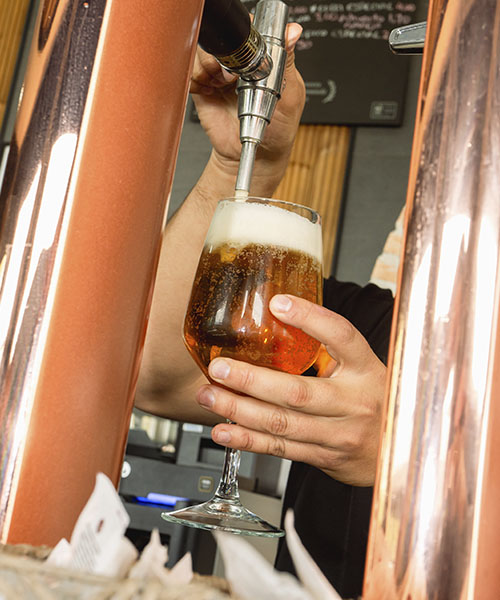 Fotografía de cerveza siendo servida en copa desde tirador, tomada por La Pecera como parte de la identidad visual de marcas de hostelería y bebidas.